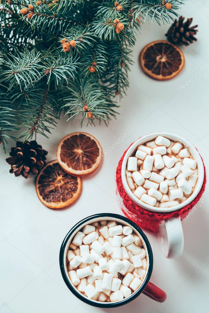 top view of cups of hot chocolate with marshmallows and pine tree branches on white surface, christmas breakfast concept