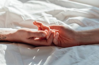 partial view of couple in live holding hads while lying in bed together