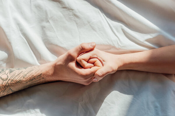 partial view of couple in live holding hads while lying in bed together