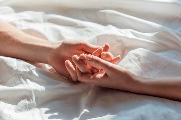 partial view of couple in live holding hads while lying in bed together