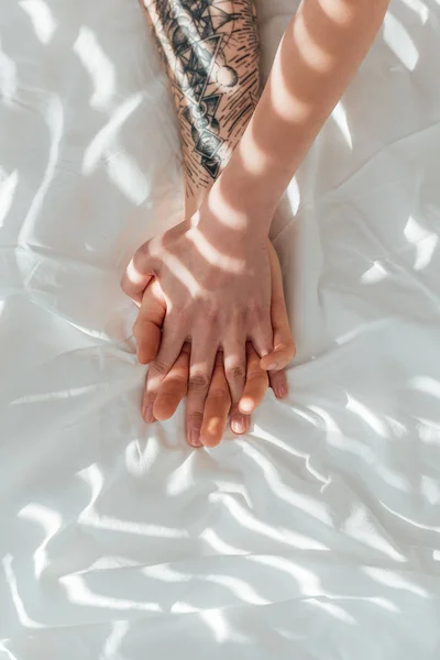 白いシーツの上に横たわるしながら手を繋いでいるカップルを愛するの部分的なビュー — ストック写真