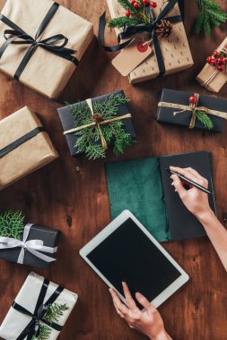 kısmi tablet ve yazma listesi günlüğüne Noel ahşap tablo kullanan kadın görünümünü sunar