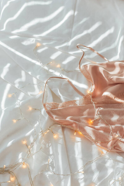 close up view of pink nightie and garland on white bed sheet