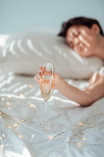 关闭的妇女拿着一杯香槟在白色床单上与花环的看法 — 图库照片