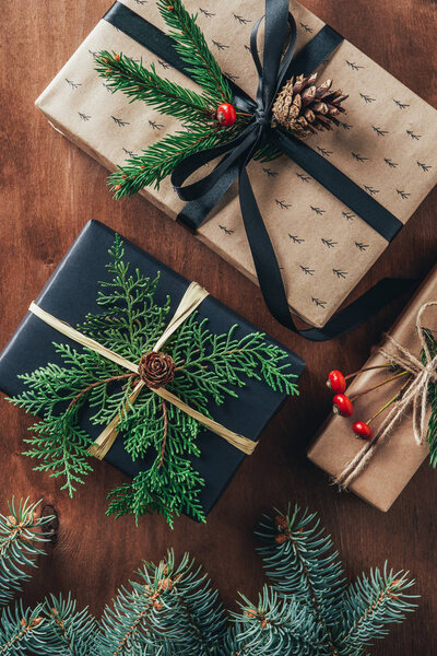 верхний вид рождественских подарочных коробок с еловыми ветвями и сосновыми шишками на деревянном фоне
  
