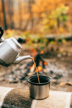coffee pouring out of metallic kettle into cup on blurred autumnal background clipart