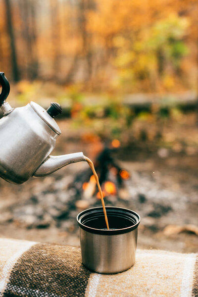 coffee pouring out of metallic kettle into cup on blurred autumnal background