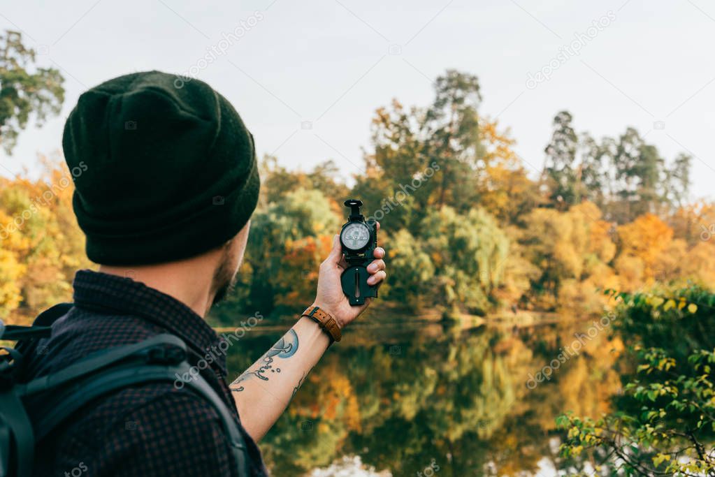 male traveller with backpack holding compass on autumnal background