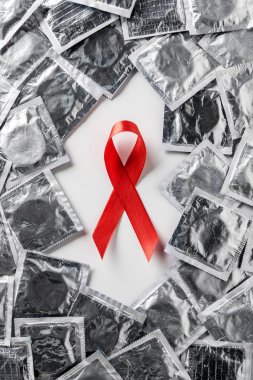 top view of aids awareness red ribbon and silver condoms on white background clipart