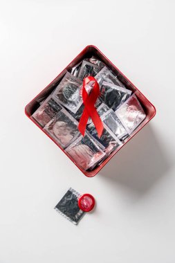 Beyaz arka plan üzerinde AIDS bilinçlendirme kırmızı şerit ve kırmızı bir kutu içinde gümüş prezervatif üstten görünüm