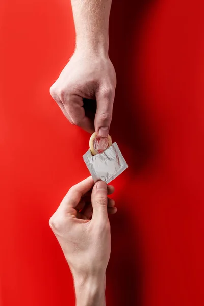 Vista Superior Das Mãos Segurando Preservativo Fundo Vermelho — Fotografia de Stock