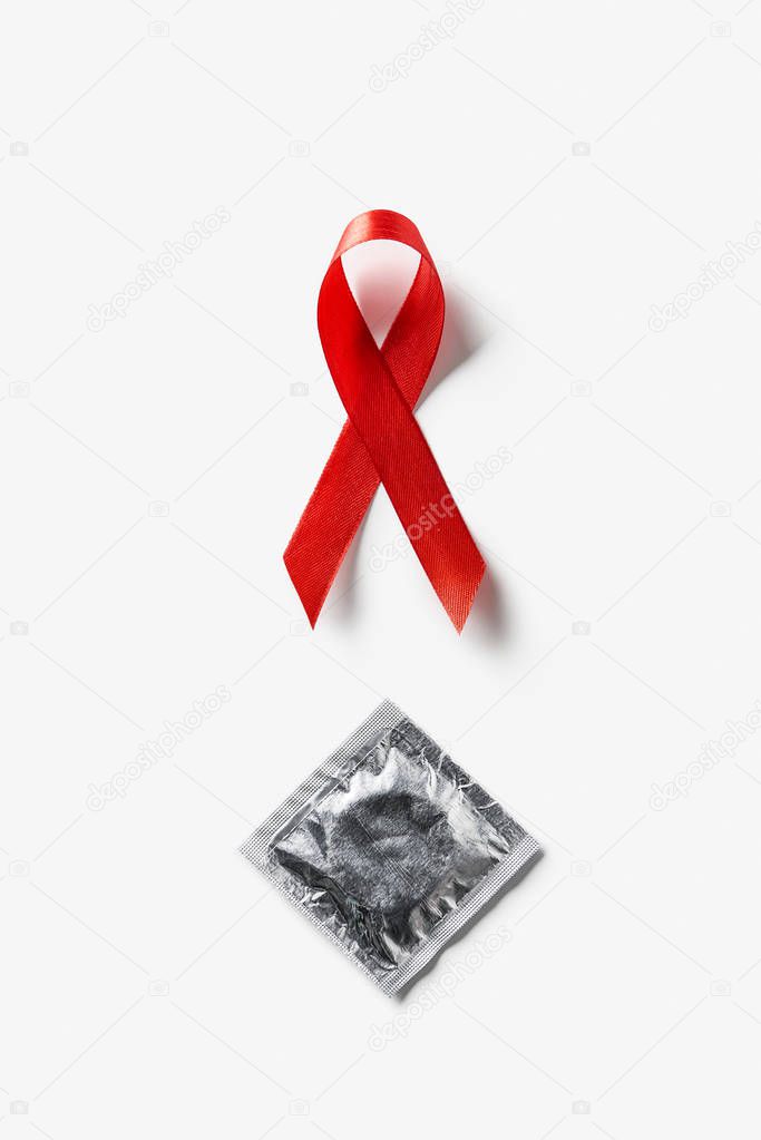 top view of aids awareness red ribbon and silver condom on white background