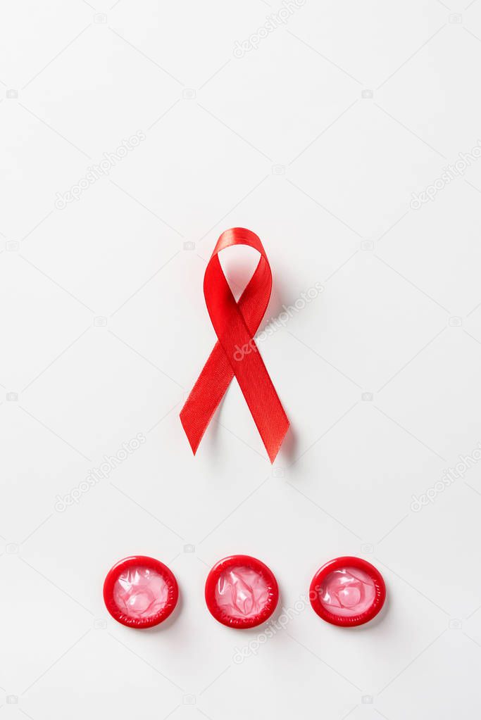 top view of aids awareness red ribbon and red condoms on white background