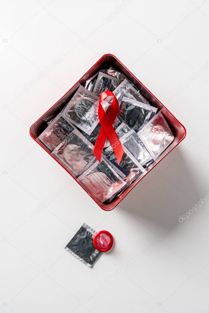 top view of aids awareness red ribbon and silver condoms in red box on white background