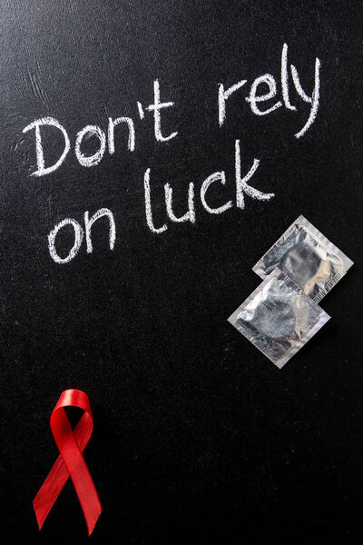 top view of aids awareness red ribbon and silver condoms on black background