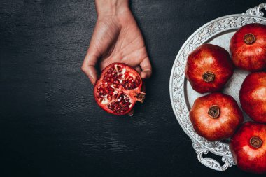 kısmi görünümünü yarısı Granat ile metal tepsi sağlıklı nar tam siyah yüzey üzerinde elinde tutan kadın
