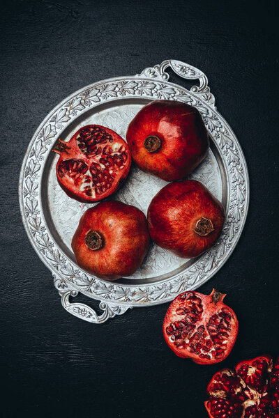 flat lay with fresh pomegranates on metal serving tray on black tabletop