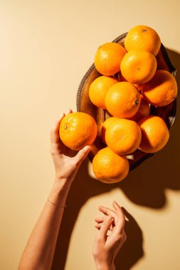 Mandalina metal kase ile bej renkli arka plan üzerinde tutan kadın görüntüsünü kırpılmış