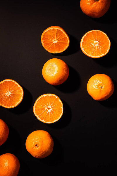 top view of arrangement of wholesome and cut tangerines on black background