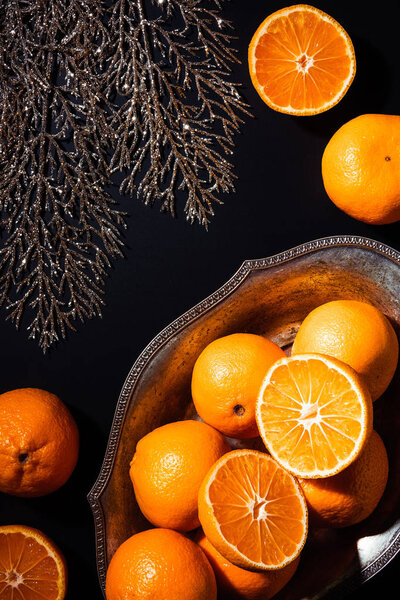 flat lay with mandarins, decorative twig and metal bowl on black backdrop