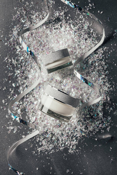 elevated view of festive ribbons and beauty cream with decorated shavings on silver