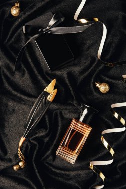 siyah kumaş üzerine parfüm, dekoratif tüyler, altın şeritler ve Noel baubles üstten görünüm