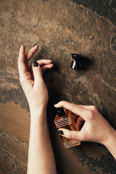 partial top view of woman applying perfume above brown weathered surface