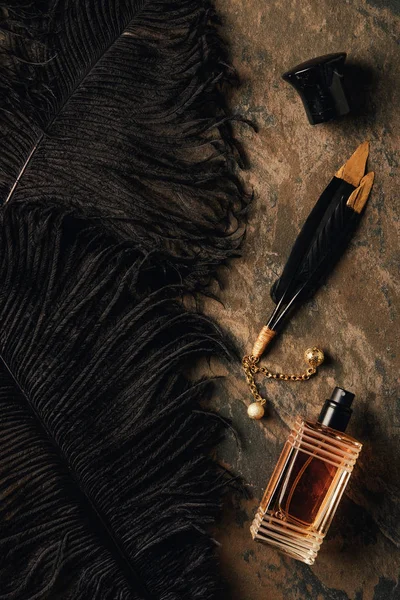 香水瓶和装饰黑色羽毛在棕色风化表面 — 图库照片