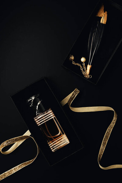 top view of perfume bottle with golden ribbon, gift box and decorative feathers on black