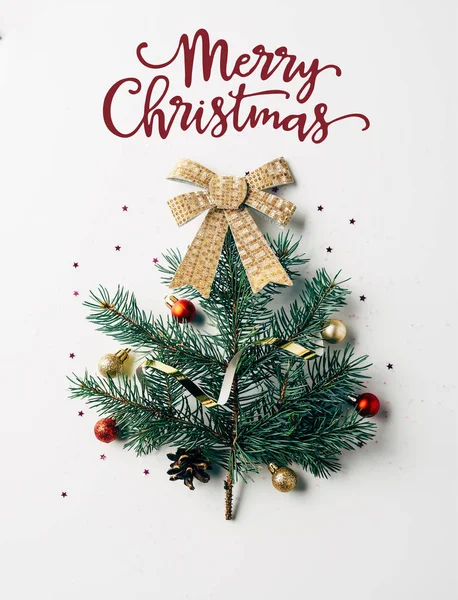 メリー クリスマス の文字と白い背景にリボン付きのお祝いクリスマス ツリーとして飾られた緑の松の枝の上から見る — ストック写真