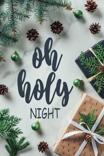 top view of christmas gift boxes with fir branches and pine cones on marble background with "oh holy night" lettering