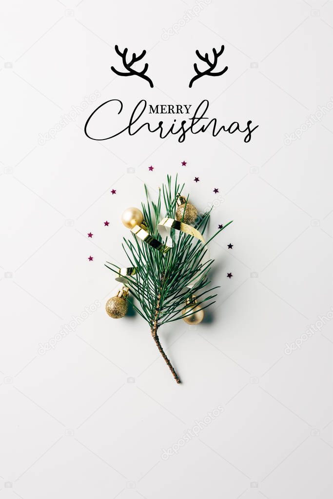 top view of little pine tree branch with ribbon and christmas balls on white surface with 