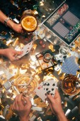 abgeschnittenes Bild von Frauen, die am Tisch mit Whiskey, alkoholischen Cocktails und Zigaretten und goldenem Konfetti pokern 