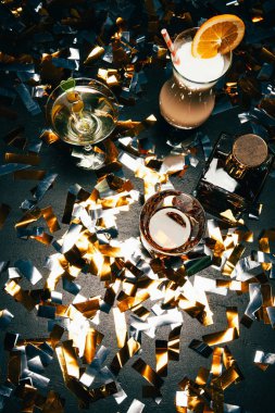 view from above of whiskey, alcoholic cocktails with orange slice and olives on table covered by golden confetti  clipart