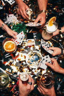 cropped image of friends with alcoholic cocktails playing poker at table covered by golden confetti  clipart