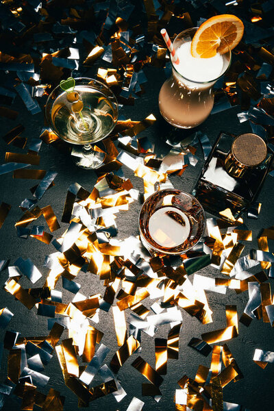 view from above of whiskey, alcoholic cocktails with orange slice and olives on table covered by golden confetti 