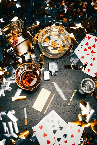 从上面看 桌上有金彩纸屑的扑克牌 威士忌 卷钞票 信用卡和可卡因 — 图库照片