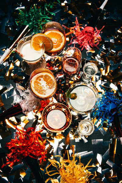 top view of various alcoholic cocktails and party horns on table covered by golden confetti 