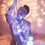 Mujer en pijama sentada en la cama con luces de Navidad alrededor