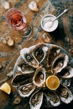 flat lay with glass of wine, oysters with ice and lemon pieces on grungy tabletop clipart