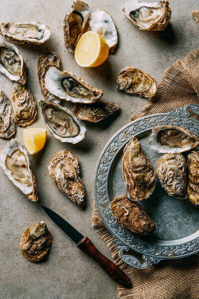 flat lay with oysters, lemon, knife and sack cloth on grey surface