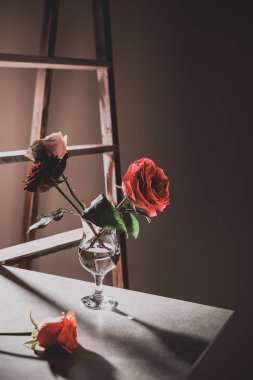 arka plan üzerinde ahşap merdiven ile şarap cam taş masada kırmızı gül çiçekler