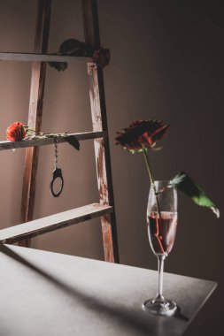 Ahşap merdiven ve arka plan üzerinde metal kelepçe ile taş tabloda şampanya cam kırmızı gül çiçek