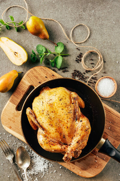top view of fried chicken in frying pan with pears and greenery