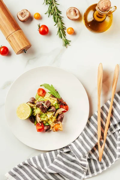 top view of salad on white plate with bottle of oil, cherry tomatoes and rosemary