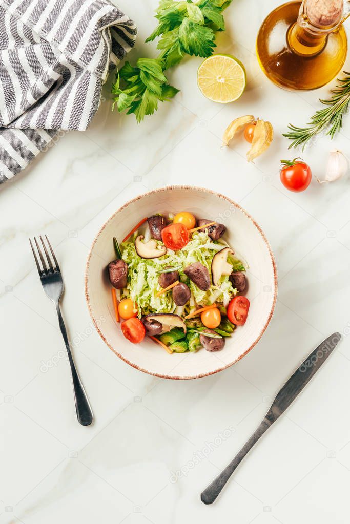 salad on white bowl with bottle of oil, cherry tomatoes, lime and rosemary on surface 
