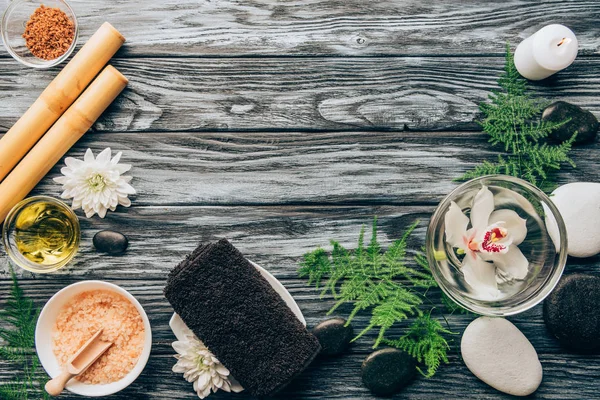 Vista superior de seixos arranjados, sal, óleo, paus de bambu e flor de orquídea em tigela para spa e massagem em fundo de madeira — Fotografia de Stock