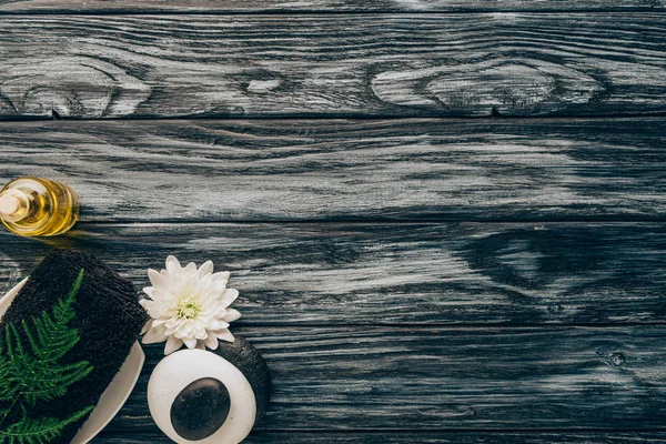 Top view of arranged spa and massage accessories with towel, pebbles, essential oil and chrysanthemum flower on wooden background — Stock Photo