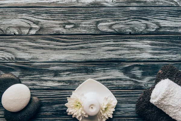 Vista superior de toallas arregladas, guijarros, velas y flores de crisantemo para spa y masaje sobre fondo de madera - foto de stock