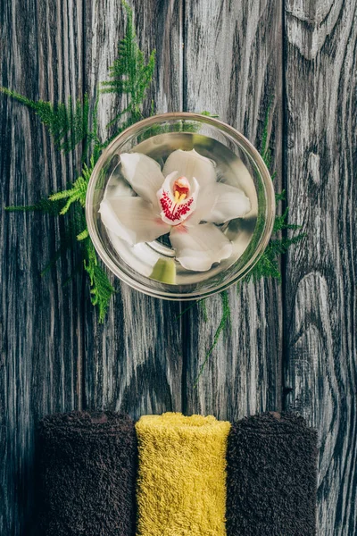 Vue de dessus de fleur arrangée d'orchidée dans le bol et serviettes pour le massage et le spa sur la surface en bois — Photo de stock